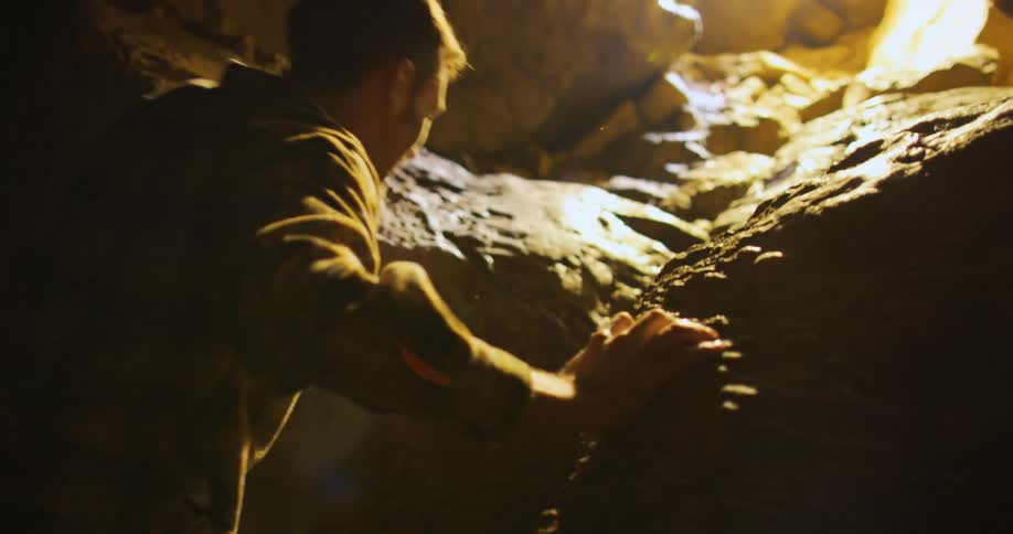 A man climbs a rocky slope in a cavern to reach the exit