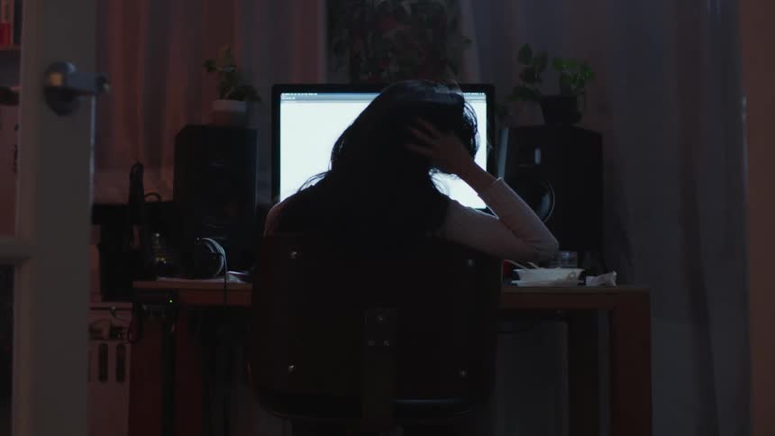 Woman sitting at desk looks at computer screen at night in room