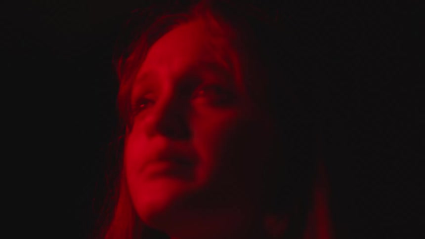 A young woman looks distressed as she stands in the dark and a light flashes overhead
