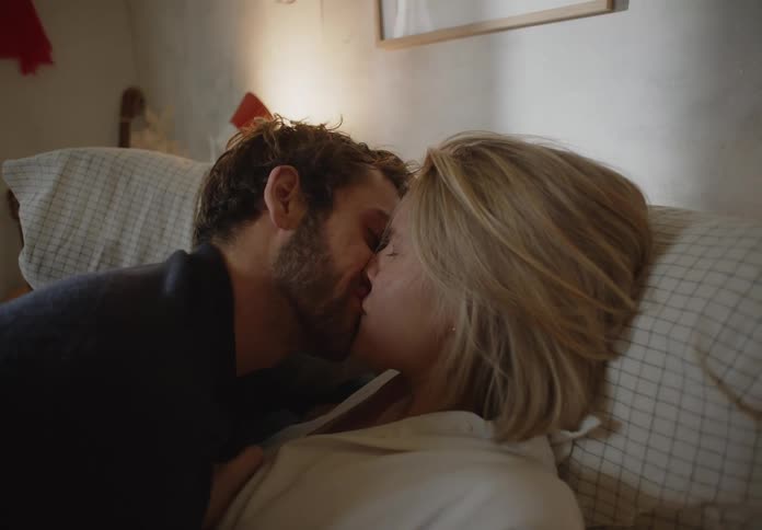 Man kissing woman in bed leans back