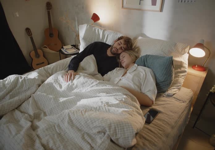 A young couple are asleep in their bedroom under a blanket in the morning
