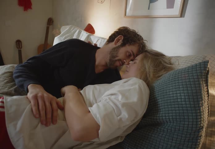 Man and woman are kissing and laying on a bed