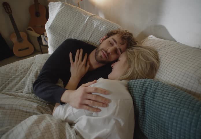 A young couple is laying down together in there bed