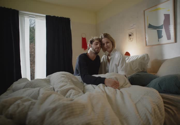 A couple is sitting close together on their bed in their night clothes in the morning
