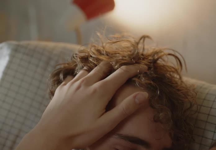 Blonde womans hand touches mans hair lying in bed in bedroom