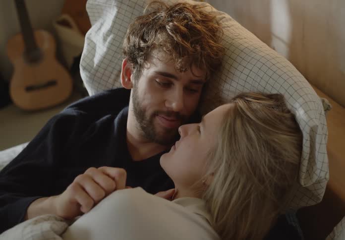 Couple lying on bed touches and looks into each others eyes in bedroom