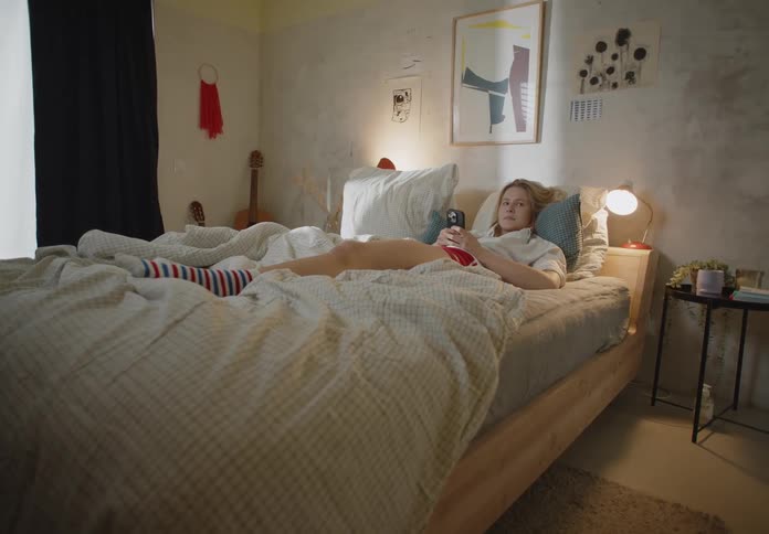 Woman lying in bed with smartphone looks over and starts to smile slightly