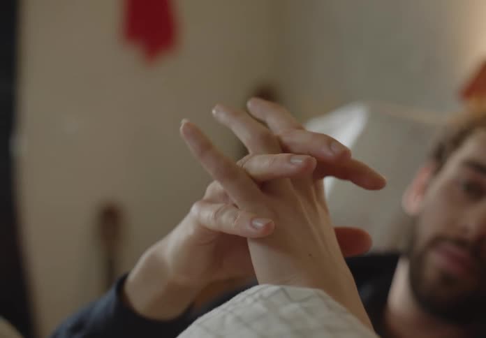A man and woman hold hands while resting in bed during the day