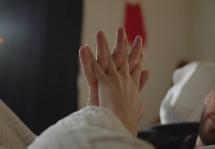 A man and woman lay in bed while holding hands