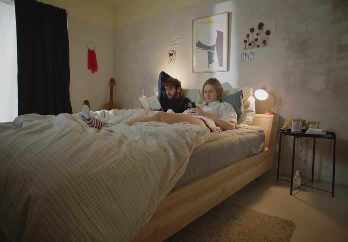 A young couple are reclining on their bed while reading during the daytime