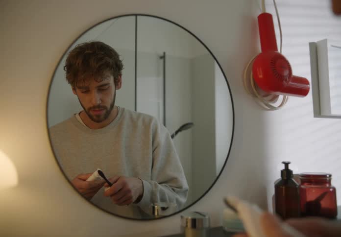 A man is standing in front of a mirror in the bathroom while preparing to brush his teeth in the morning