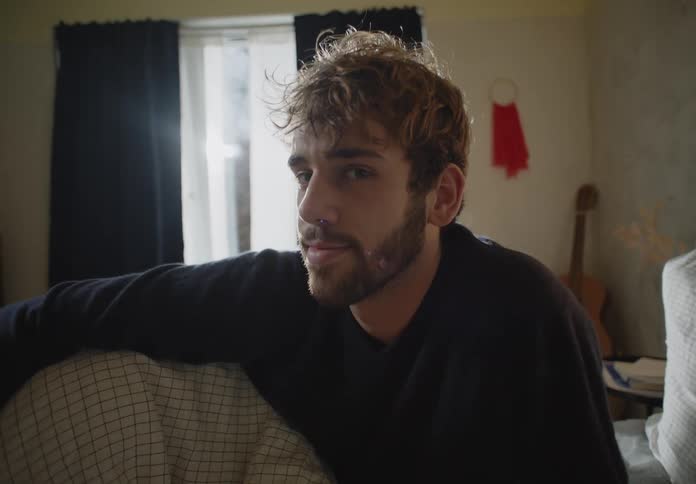 A young white man is sitting in his bed around morning time