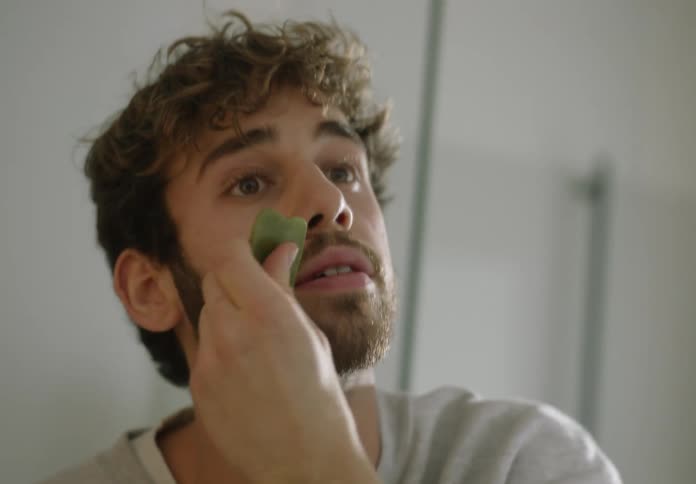 A man doing his skincare routine with a jade stone