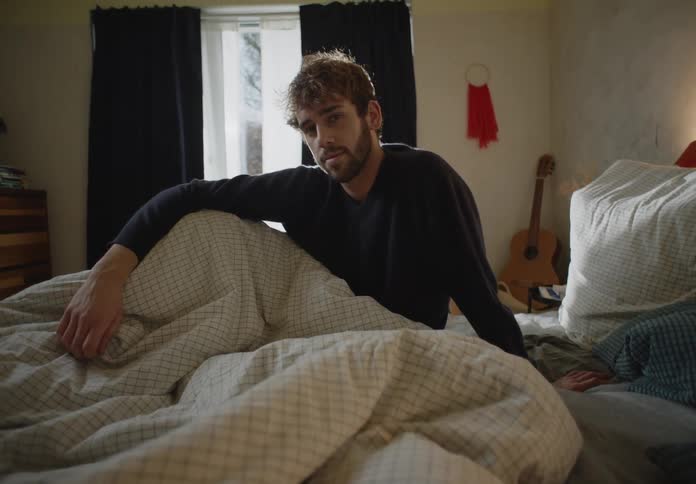 A man is sitting on his bed during the daytime