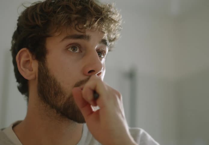 A man is looking into a bathroom mirror while brushing his teeth in the daytime