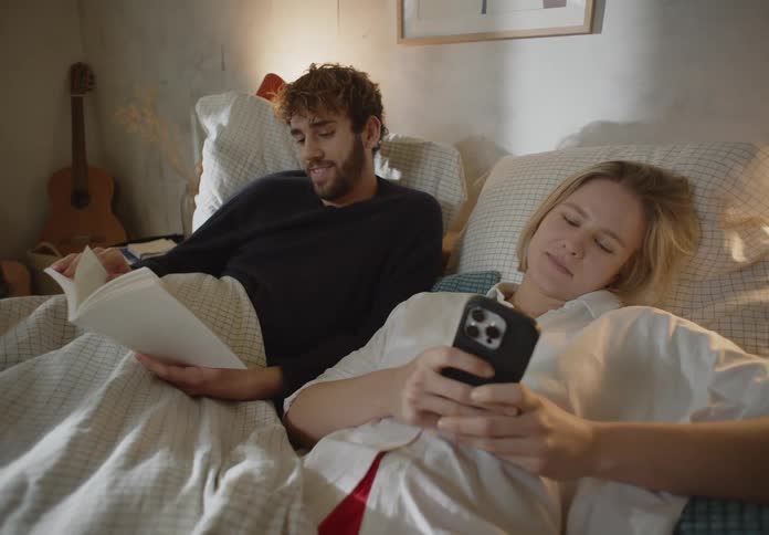Man and woman are texting and reading a book while laying in bed
