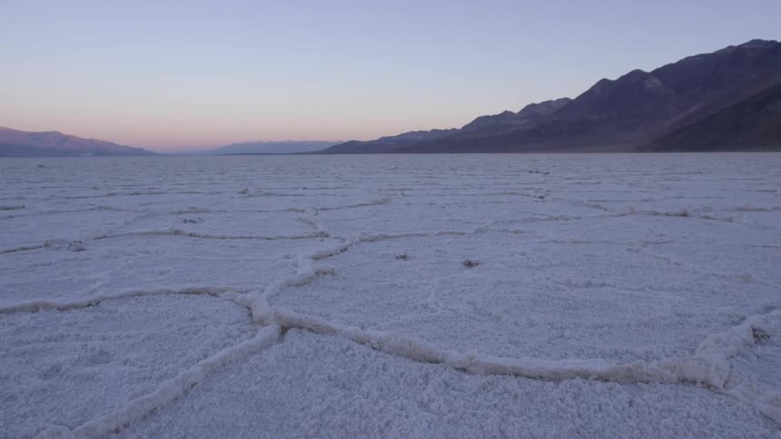 A snow covered pasture at the foot of a mountain range during sunset
