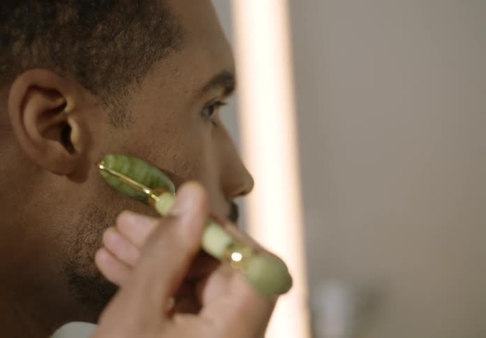 A man is smoothing his skin with a jade roller