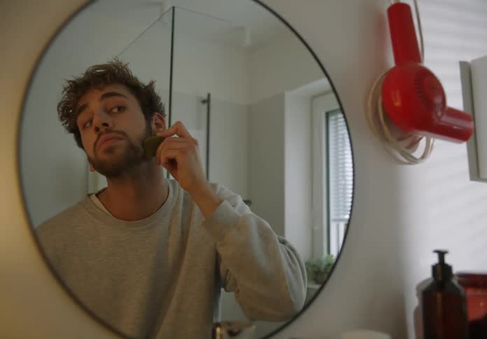 A man rubbing something on his beard and face in the bathroom mirror