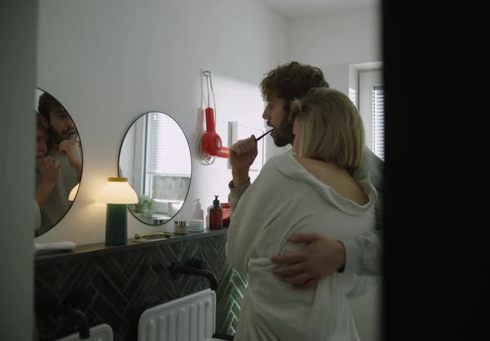 Young couple is in the bathroom and man is brushing his teeth