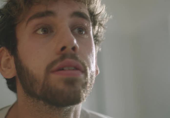 A bearded man wipes his face with his hands and a towel in front of a mirror