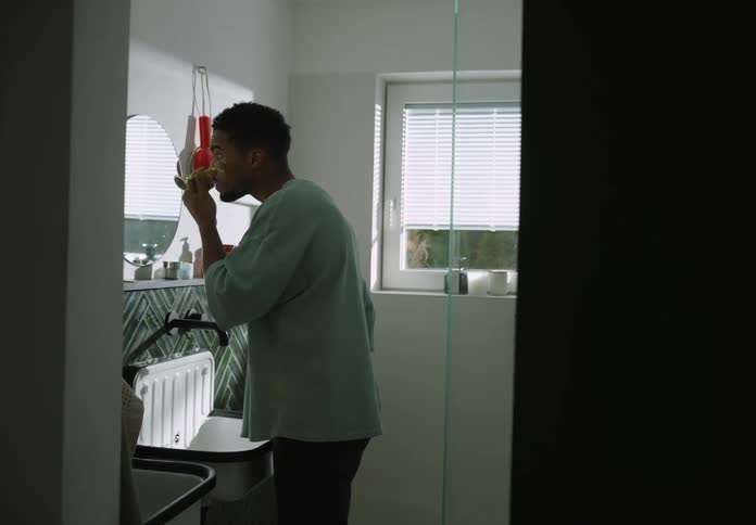 A black man uses a jade roller on his face while looking into a bathroom mirror