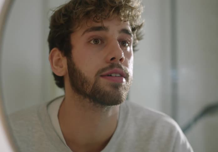 A young man is looking in the mirror in the bathroom