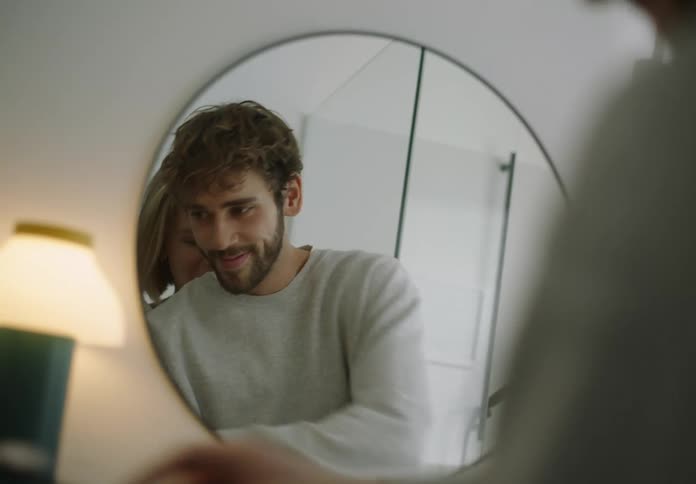 A man and woman stand in a bathroom looking in the mirror