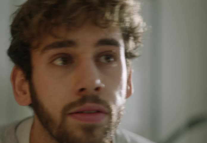 A man walks toward a bathroom mirror and touches his face