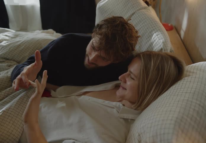 A man and woman touch hands together in bed