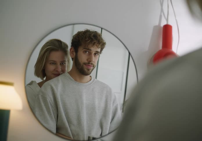 A woman hugs her partner from behind while standing in front of a bathroom mirror