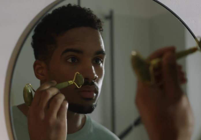 A man is smoothing his skin while looking in a mirror