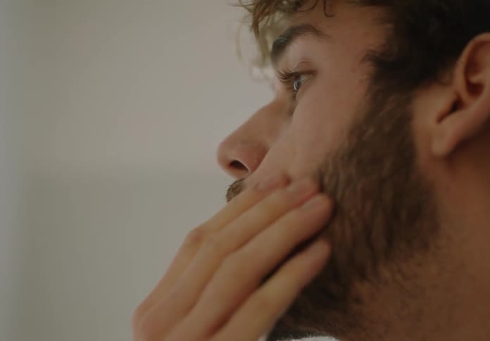 A young white man is touching his face