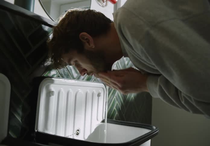 A man is standing over the bathroom sink using his hands to splash water onto his face