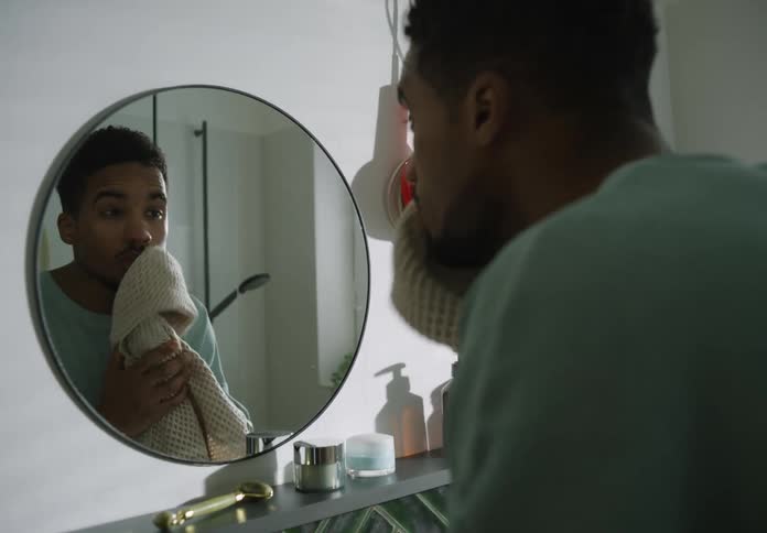 A man dries his face with a towel while looking in the mirror