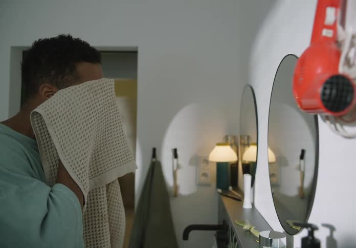 A young man is looing in the mirror in the bathroom