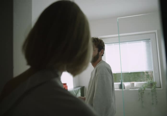 A woman joins her partner in the bathroom and hugs him from behind
