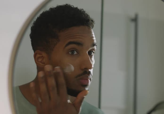 Man with beard applies face cream in bathroom