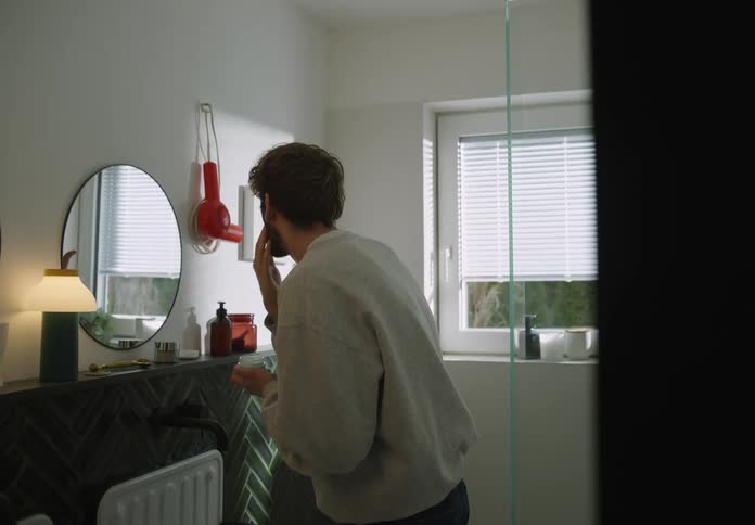 A man is standing in the bathroom and applying face cream
