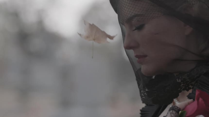 A woman in a black mourning veil holds a red rose to her chest