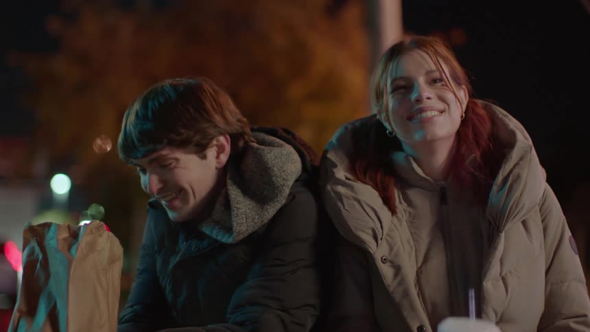 A couple laugh while eating fast food outside at night