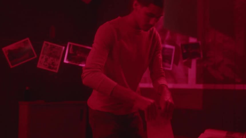A young man develops photographs in a dark room