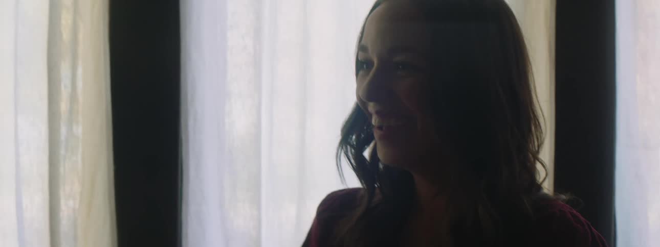 Woman laughs in dimly lit room near curtained windows