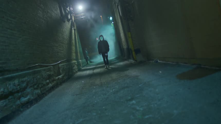 Person wearing digital mask displaying different images walks through lighted alley on a foggy night