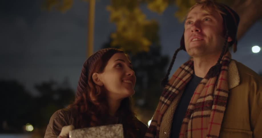 A couple walk together while carrying wrapped gifts into a home