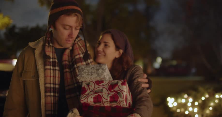 A couple man and woman walking down the street carrying presents and laughing