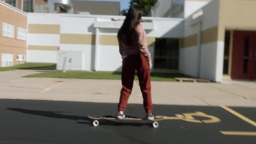 A girl falls off her skateboard while riding through a parking lot