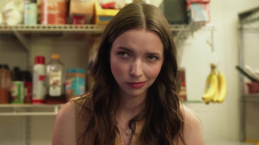 A woman eating something off a spoon looking up and giving a disgruntled expression