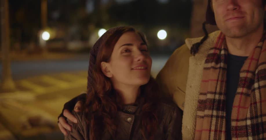 A couple of lovers kissing and looking at something while smiling then walking down the city street at night