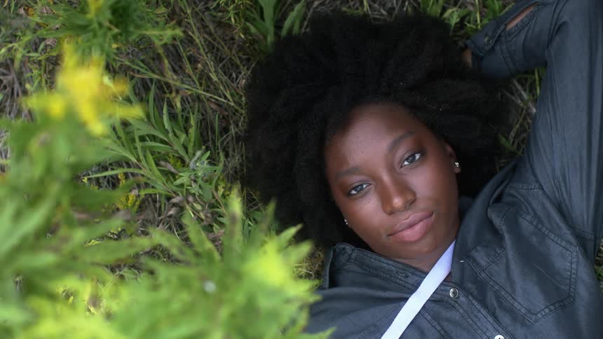 A woman is lying on the ground looking up as plants move in the breeze